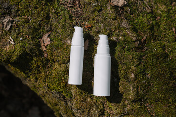 A dark and light glass serum bottle with a dropper, tree bark wood, moss. forest on a sunny day nature background. Concept of skin care, hydration, cosmetic demonstration eco-friendly product mock up