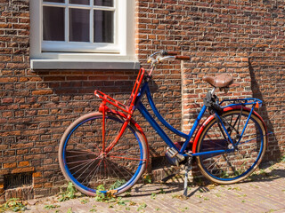 Fototapeta premium Red and blue painted bicycle leaning against brick wall in Leiden street, urban lifestyle and cycling culture concept