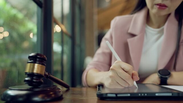 Woman consulting legal documents remotely using digital tablet and stylus with gavel in the scene
