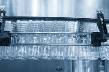 The  empty drinking water bottles  hanging on the overhead conveyor belt for filling process in the light blue scene.