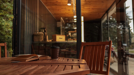 Coffee cup and book on a wooden table outside a coffee shop