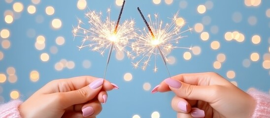 Two hands hold sparkling fireworks against a soft blue bokeh background
