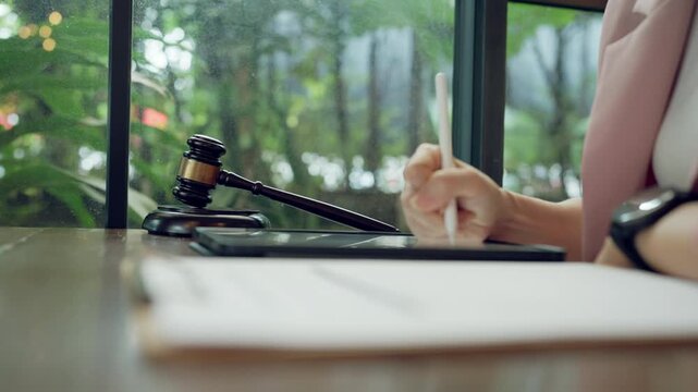 Close-up of law student or trainee lawyer writing legal content on tablet next to gavel, symbol of justice