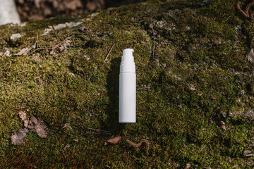 A dark and light glass serum bottle with a dropper, tree bark wood, moss. forest on a sunny day nature background. Concept of skin care, hydration, cosmetic demonstration eco-friendly product mock up