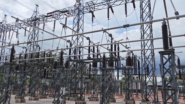 Pan right of high voltage electrical substation switchyard structures against blue sky for energy infrastructure.