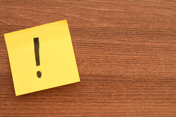 Exclamation Mark Sticky Note. Yellow sticky note with black exclamation mark on wooden desk...