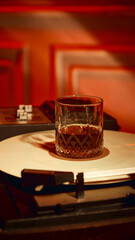 Glass of whiskey placed on vinyl record under warm red light. Concept of luxury lifestyle, psychology of emotions, nightlife branding, bar culture, and evening relaxation.