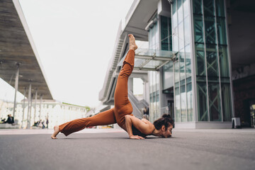 Young woman in advanced yoga forearm balance variation on pavement, leg lifted behind. Conceptual stock image symbolizing empowerment, mindfulness, resilience, strength, and wellness.