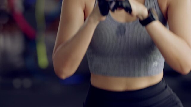 Focused Asian woman exercising in gym wearing gloves. Sweat shows dedication. Emphasis on fitness, mental strength, healthy living.