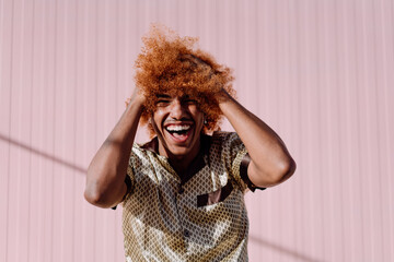 Cheerful African American man with curly ginger afro laughing with hands on head, wearing silk...