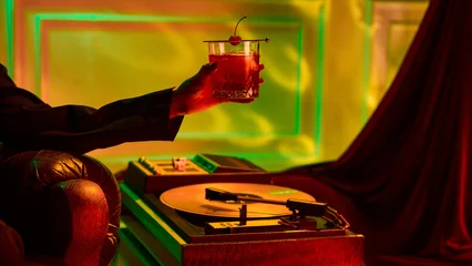 Wandcirkels Bar Elegant cocktail with cherry held in hand beside vintage record player in warm neon light. Concept of entertainment marketing, lifestyle advertising, luxury emotions, and music branding.  © master1305