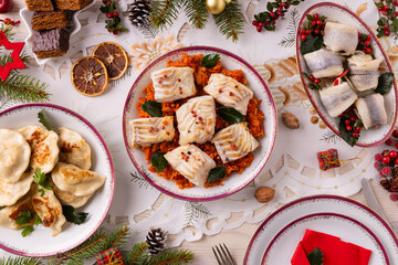 Classic Christmas food medley on a decorated table. Fish, dumplings stuffed with cabbage and mushrooms, cheesecake, and ham.