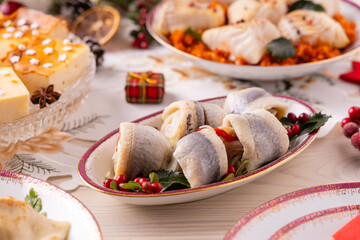 Classic Christmas food medley on a decorated table. Fish, dumplings stuffed with cabbage and mushrooms, cheesecake, and ham.