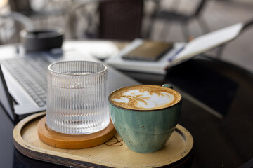A cup of coffee and a glass of water sit on a wooden tray next to a laptop.