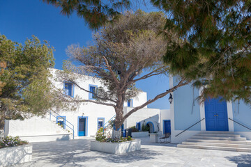 Beautiful Greek Orthodox chapel of Panagia Kastriani, in Kea island, with a blue dome and bell tower, framed by trees against a clear blue sky.