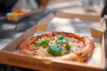 Fresh pizza with basil leaves in open box