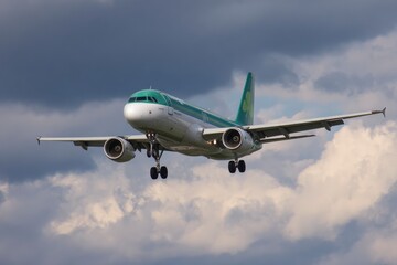 An Aer Lingus airplane descends with landing gear deployed against a cloudy sky