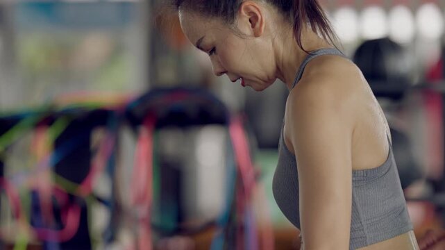 Focused and strong Asian woman performing lateral raise dumbbell exercise at gym. Training for strength and endurance.