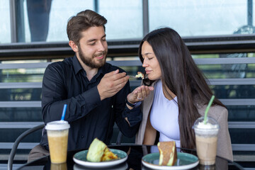 The man is feeding the woman a piece of dessert from a plate while