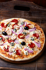 Pizza with chorizo ​​sausage, mozzarella cheese, and black olives. Rustic wooden background. Soft focus.	