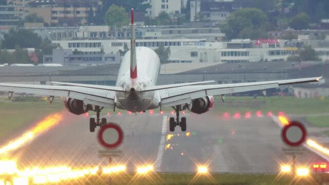 Commercial passenger airplane landing on an illuminated airport runway strip. Ground level, rear of the plane point of view, touchdown and taxi, real time, super-telephoto, cloudy, no people