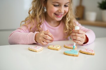 Young girl decorating heart shaped cookies with colorful icing and sprinkles, smiling and enjoying creative baking activity in bright kitchen setting