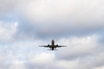 A passenger airplane with its landing gear down is approaching for landing in a cloudy sky.