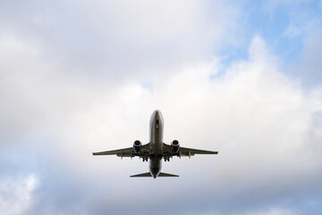 A passenger airplane with its landing gear down is approaching for landing in a cloudy sky.