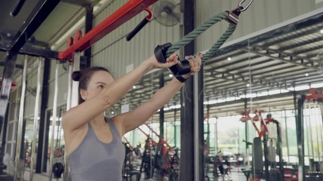 Focused Asian woman using cable rope machine to perform face pull exercise. Strength and fitness training for upper body.