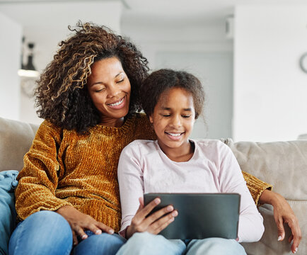 Teenage girl sitting at sofa with her mother and using tablet computer. Mother and daughter bonding and having fun at home