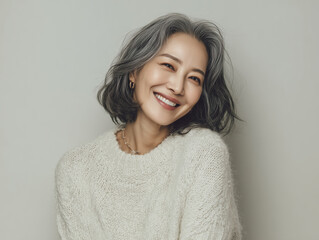 グレーヘアの美しい女性が白いニットで微笑むポートレート