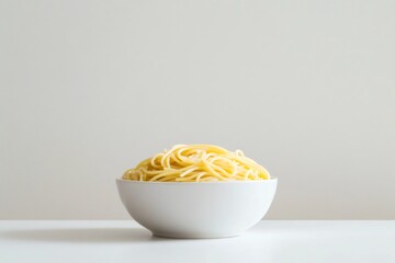 Simple white bowl filled with a mound of cooked spaghetti sits on a white table against a neutral background, creating a minimalist food image