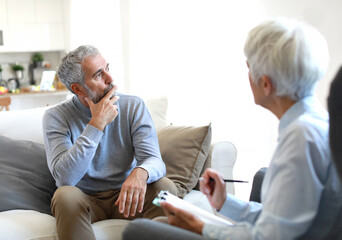 Portrait of a senior mature or mid aged man looking thoughtful or stressed and sad while sitting in session with his female therapist