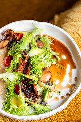 Gourmet salad with grilled octopus, avocado, cherry tomatoes, frisée, microgreens, and artistic sauces on a white plate. Fine dining presentation, top view
