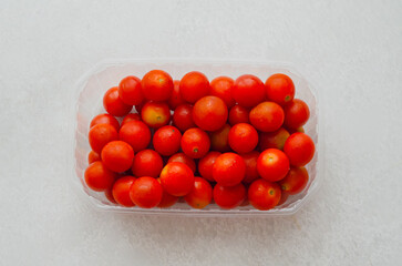 Cherry tomatoes in plastic container top view on light background