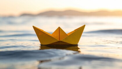 A yellow paper boat floats on calm water with a blurred sunset background.