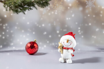 A toy figure of a snowman holding a star and a Christmas tree ball on a festive snowy background. Christmas celebration concept, greeting card