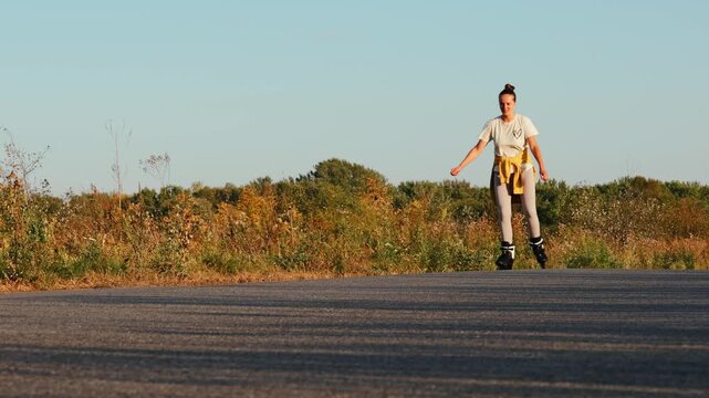 Woman enjoying roller skating on a peaceful country road as the sun sets, surrounded by colorful foliage and clear blue skies