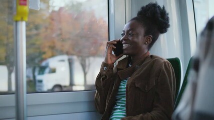 African American woman sitting on bus laughing during phone conversation. Passenger holding smartphone close to ear enjoying remote communication. Modern technology connecting people while commuting. - Powered by Adobe