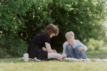 Fototapeta premium A young mother and her son with hearing aids enjoy a joyful picnic in nature, sharing authentic moments of outdoor play and unconditional love. Unaltered, genuine family connection