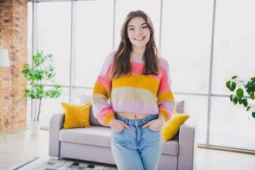 Smiling young woman wearing a colorful sweater in a cozy living room with a modern design and natural lighting