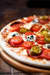 Pizza with salami, jalapeno pepper, cherry tomatoes and mozzarella cheese. Soft focus.	