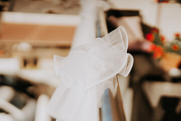 A white bow made of tulle is elegantly tied to a railing in a warmly lit indoor space. The...