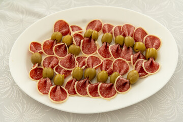 Delicious slices of salami are neatly arranged on a white platter, interspersed with green olives. This savory appetizer is perfect for a social event or gathering.