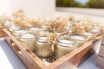 A beautiful wooden tray holds small glass candles decorated with dried flowers. The sun shines brightly, creating a warm and inviting atmosphere for relaxation.