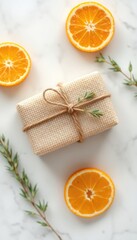 Elegant gift wrapped in natural linen with twine, accented with fresh rosemary sprigs and bright orange slices on marble