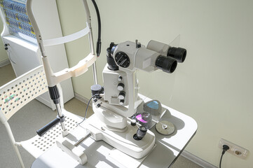 A slit lamp biomicroscope for eye examinations sits on a table in a bright medical setting