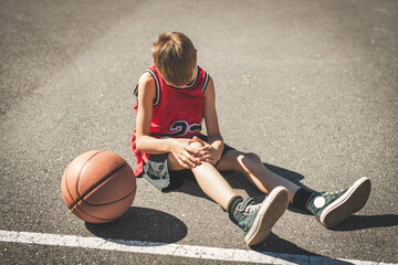 young boy playing basketball on a court, the boy having knee injury and crying