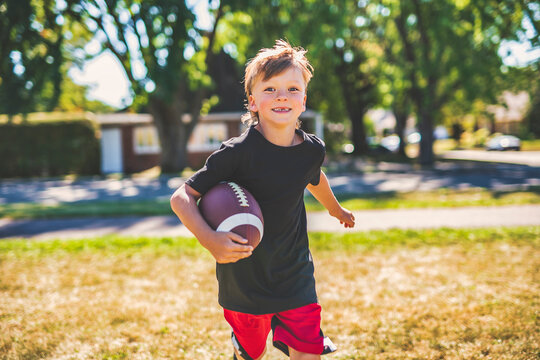 child boy playing American football. Kid play football in sunny summer park. - Powered by Adobe