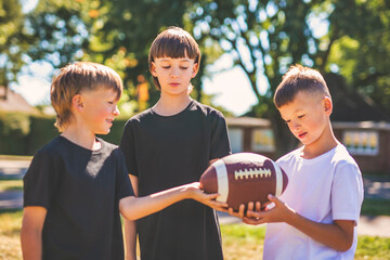 brother playing American football. Kids play football in sunny summer park.